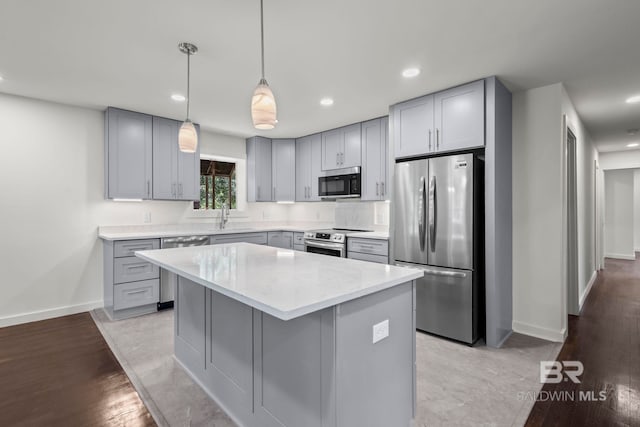 kitchen featuring a sink, a center island, stainless steel appliances, baseboards, and gray cabinetry