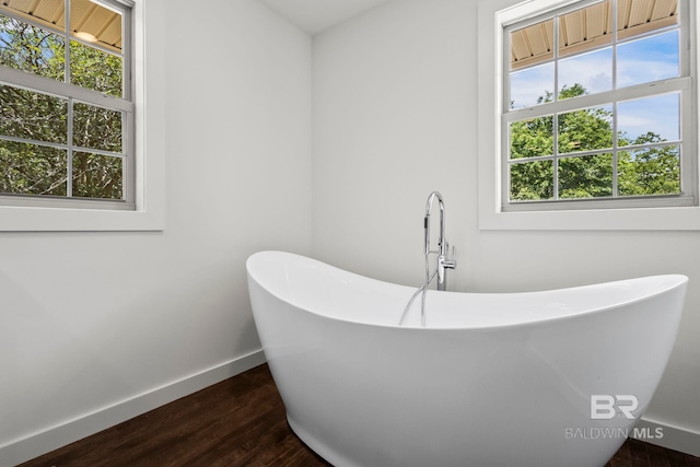 bathroom with baseboards, a freestanding bath, a wealth of natural light, and wood finished floors