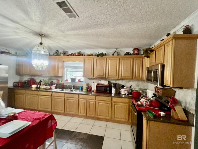 kitchen featuring appliances with stainless steel finishes, a sink, dark countertops, a textured ceiling, and decorative light fixtures