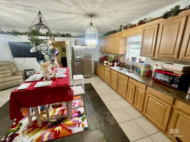 kitchen with a sink, stainless steel refrigerator with ice dispenser, a chandelier, light tile patterned flooring, and decorative light fixtures