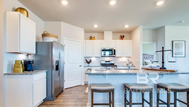 138 Preston Way, Gulf Shores, AL 36542 - kitchen featuring appliances with stainless steel finishes, a breakfast bar area, white cabinets, decorative backsplash, and light stone counters