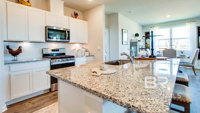 138 Preston Way, Gulf Shores, AL 36542 - kitchen with appliances with stainless steel finishes, a sink, light wood-type flooring, white cabinetry, and light stone counters