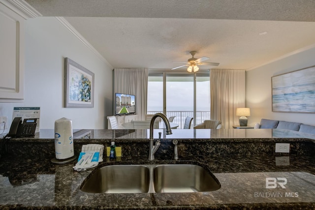 kitchen with ornamental molding, a textured ceiling, ceiling fan, sink, and dark stone countertops