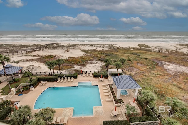 view of pool featuring a patio area, a water view, and a beach view