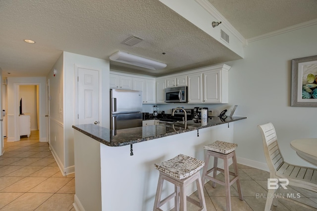 kitchen with a breakfast bar, kitchen peninsula, a textured ceiling, white cabinetry, and stainless steel appliances