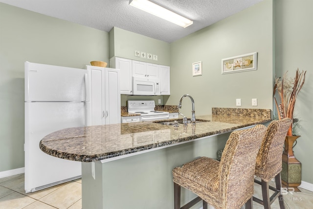 kitchen featuring white appliances, white cabinets, a breakfast bar, dark stone countertops, and a peninsula