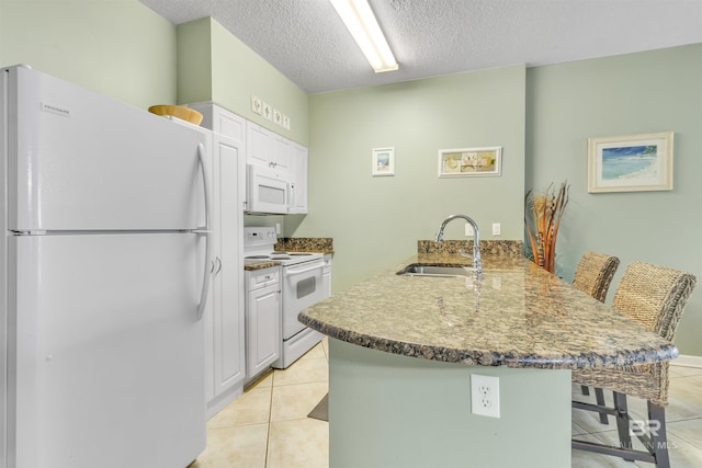 kitchen with light tile patterned floors, a breakfast bar area, a peninsula, white appliances, and white cabinetry