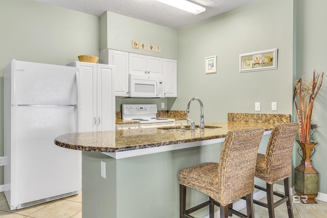 kitchen featuring white appliances, a breakfast bar, dark stone countertops, a peninsula, and light tile patterned flooring