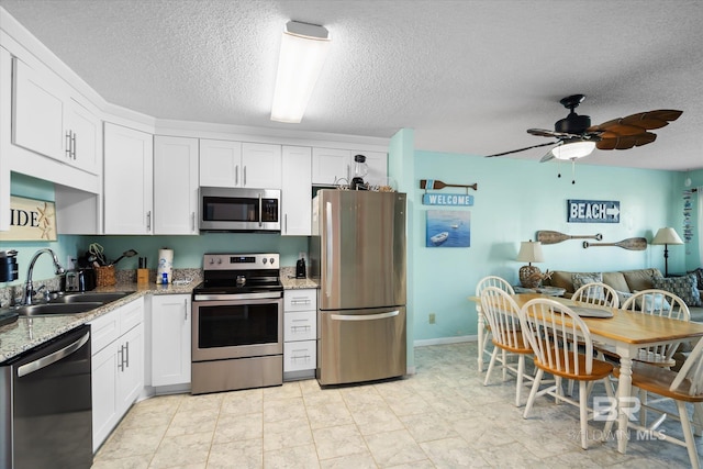 kitchen featuring appliances with stainless steel finishes, sink, a textured ceiling, white cabinetry, and light stone counters