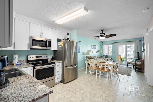 kitchen with white cabinetry, appliances with stainless steel finishes, light stone counters, a textured ceiling, and ceiling fan