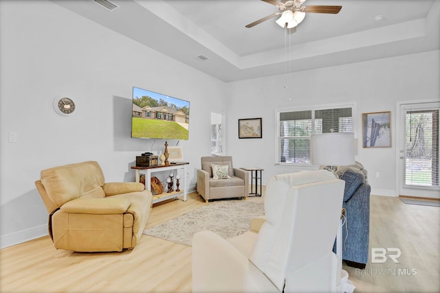 living area with baseboards, a raised ceiling, light wood-style floors, ceiling fan, and visible vents