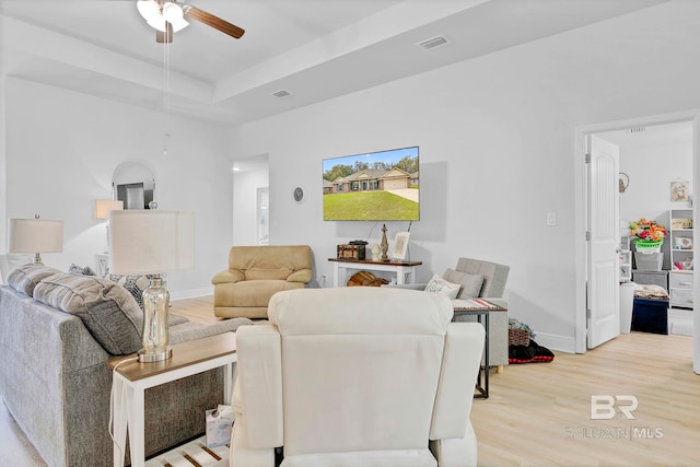 living area featuring a tray ceiling, visible vents, a ceiling fan, and light wood finished floors