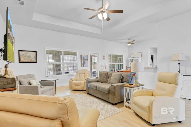 living room featuring a ceiling fan, visible vents, light wood-style floors, and a raised ceiling