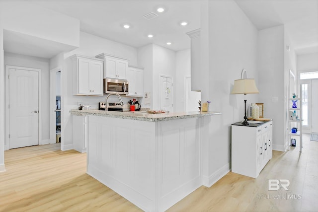 kitchen with light wood finished floors, white cabinetry, light stone countertops, stainless steel appliances, and recessed lighting