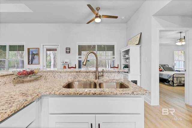 kitchen with white cabinets, ceiling fan, a sink, light wood-style floors, and light stone counters
