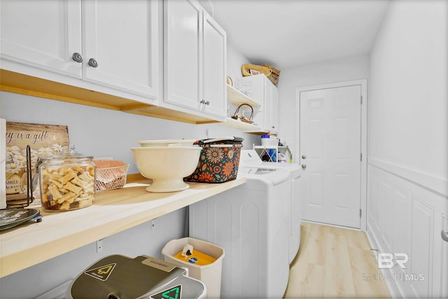 washroom featuring a wainscoted wall, separate washer and dryer, cabinet space, and light wood-type flooring