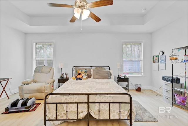 bedroom with wood finished floors, multiple windows, and a raised ceiling
