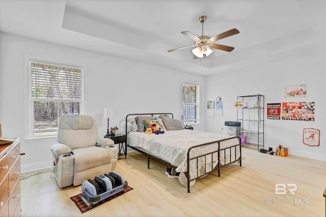 bedroom featuring a raised ceiling, baseboards, multiple windows, and wood finished floors