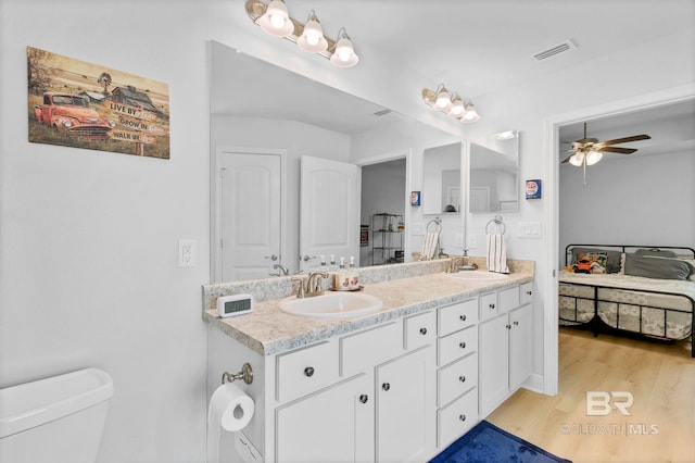 bathroom featuring toilet, a sink, ceiling fan, visible vents, and wood finished floors