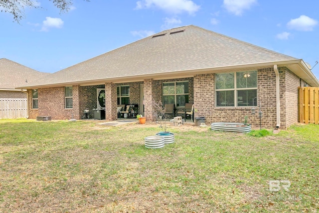 back of property with a patio area, roof with shingles, fence, brick siding, and a lawn
