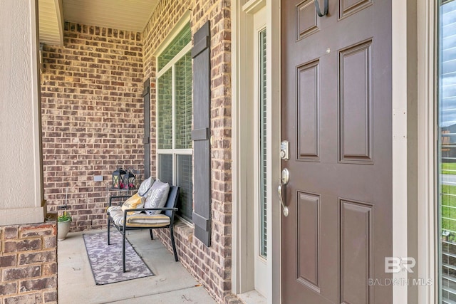 view of exterior entry with brick siding and a porch