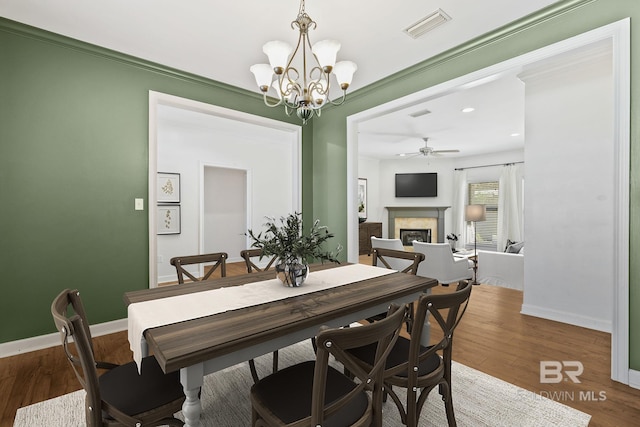 dining space featuring wood-type flooring, ceiling fan with notable chandelier, and ornamental molding