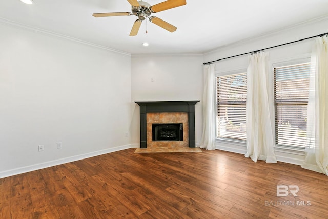 unfurnished living room featuring ornamental molding, ceiling fan, wood finished floors, a tile fireplace, and baseboards