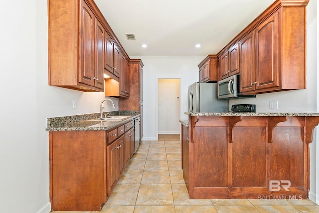 kitchen featuring visible vents, a breakfast bar area, appliances with stainless steel finishes, dark stone countertops, and a sink