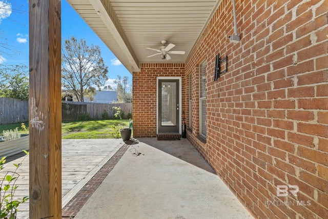 entrance to property featuring a patio, brick siding, fence, and a ceiling fan