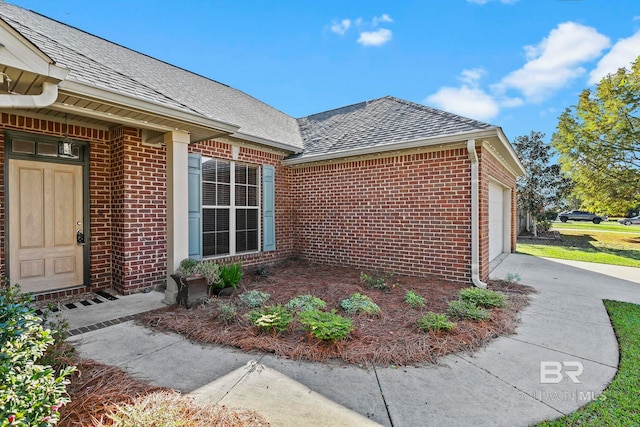 entrance to property with a shingled roof, brick siding, driveway, and a garage