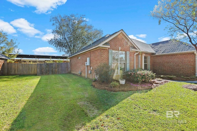 view of side of property featuring a yard, brick siding, and fence