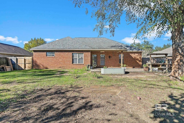 back of house featuring a gate, brick siding, a lawn, and fence