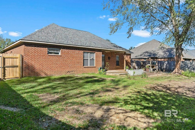 back of house with brick siding, a lawn, a fenced backyard, and roof with shingles