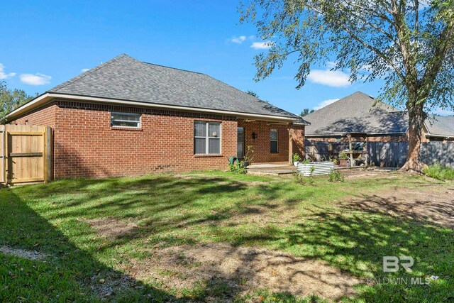 rear view of property featuring a fenced backyard, a shingled roof, a lawn, and brick siding