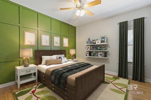 bedroom featuring a decorative wall, ceiling fan, light wood-style flooring, and baseboards