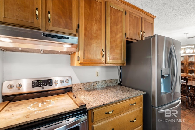 kitchen with a textured ceiling, appliances with stainless steel finishes, hanging light fixtures, and light stone countertops