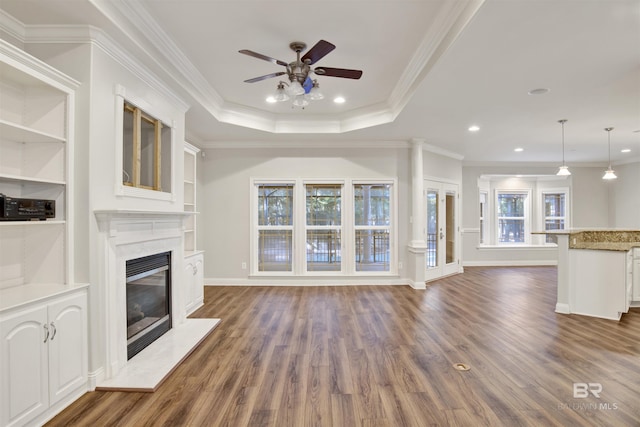 unfurnished living room featuring a high end fireplace, crown molding, ceiling fan, built in features, and a tray ceiling