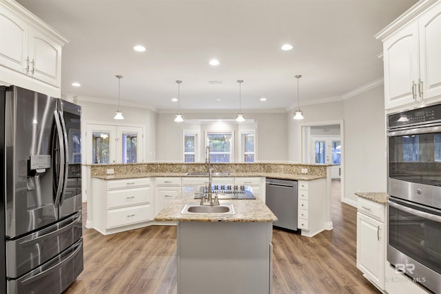 kitchen with decorative light fixtures, stainless steel appliances, white cabinetry, and a center island with sink