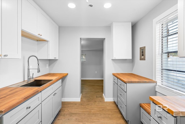 kitchen with white cabinets, light hardwood / wood-style flooring, butcher block counters, and sink