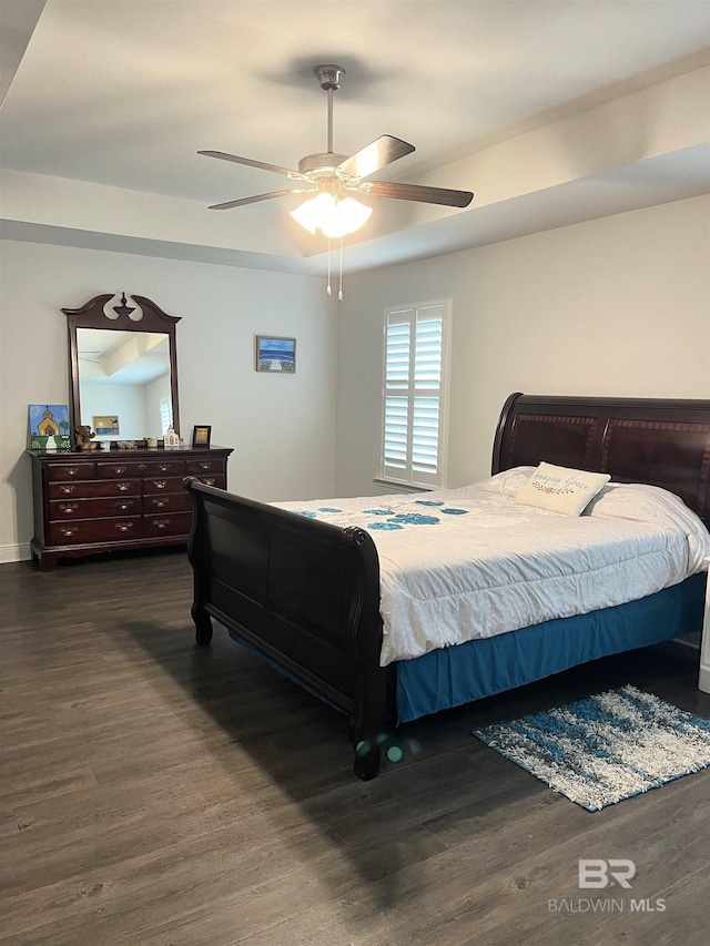 bedroom with a ceiling fan, a tray ceiling, and dark wood-style flooring