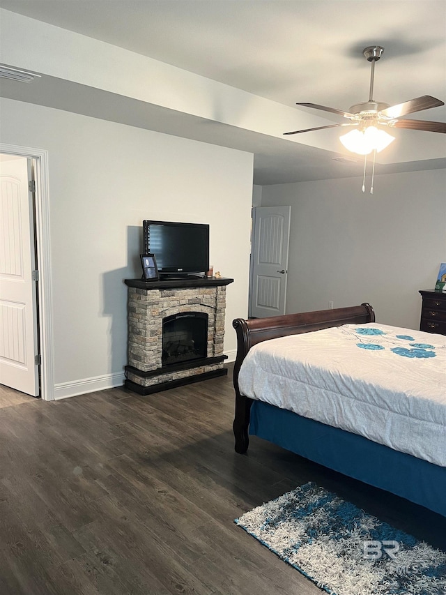 bedroom with wood finished floors, visible vents, baseboards, ceiling fan, and a stone fireplace