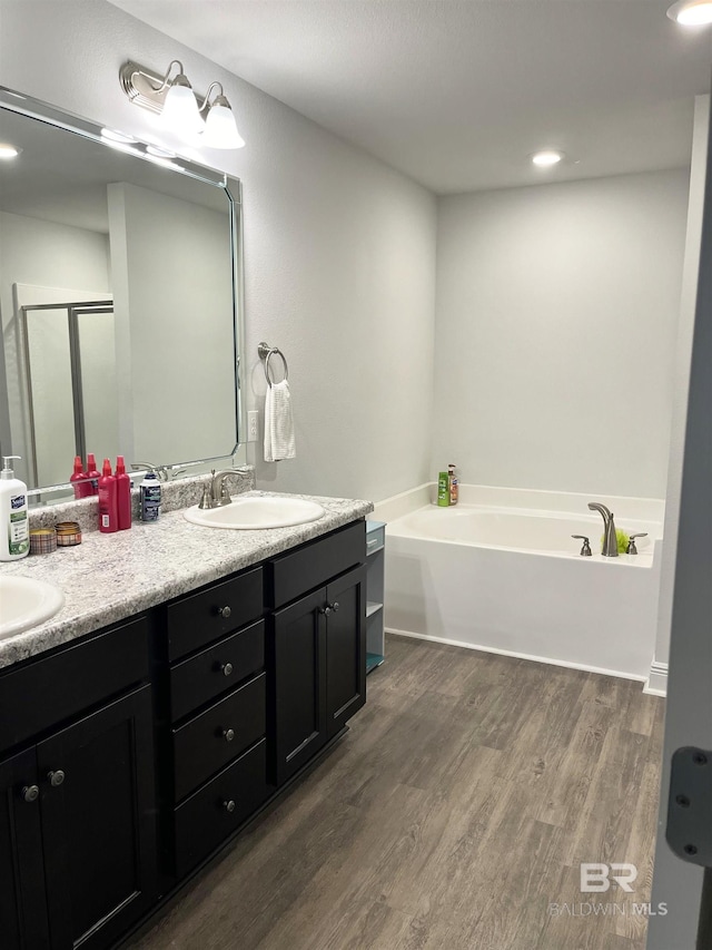 bathroom with a sink, a garden tub, wood finished floors, and double vanity