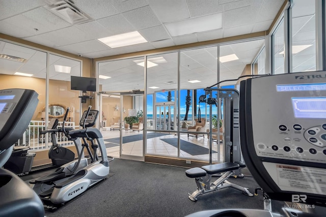 workout area with a paneled ceiling and a wall of windows