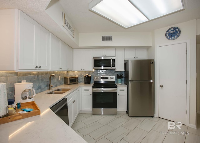 kitchen with appliances with stainless steel finishes, tasteful backsplash, sink, white cabinets, and light stone counters