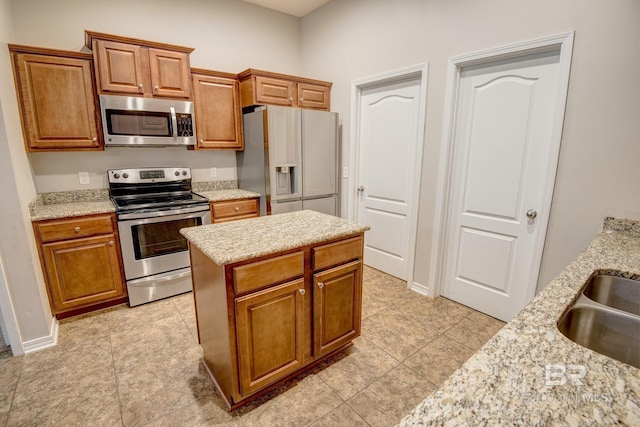 kitchen featuring light stone countertops, appliances with stainless steel finishes, sink, a center island, and light tile patterned flooring