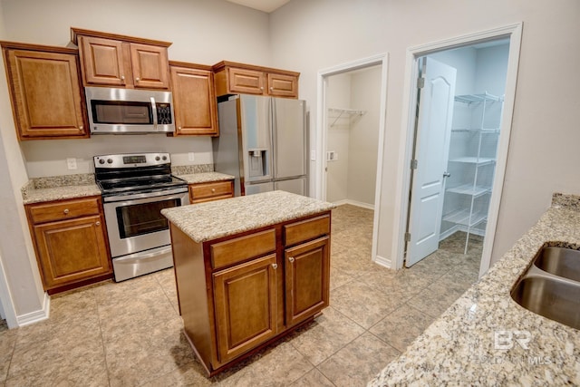 kitchen with a center island, sink, stainless steel appliances, light stone counters, and light tile patterned floors