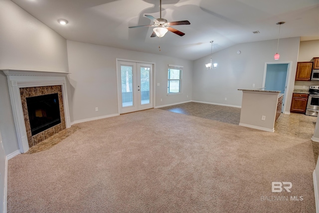 unfurnished living room with french doors, light colored carpet, vaulted ceiling, a tiled fireplace, and ceiling fan with notable chandelier