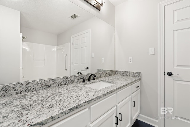 bathroom with visible vents, a textured ceiling, a shower, baseboards, and vanity