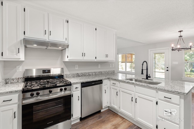 kitchen with under cabinet range hood, appliances with stainless steel finishes, a peninsula, white cabinetry, and a sink