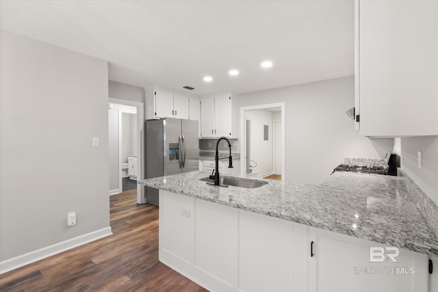 kitchen with a peninsula, a sink, white cabinetry, range, and stainless steel fridge